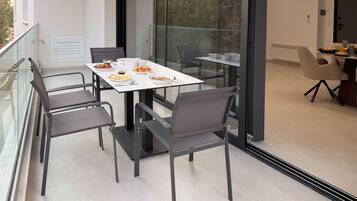 A modern dining area with a glass table and chairs, a balcony with a railing, and a view of trees.