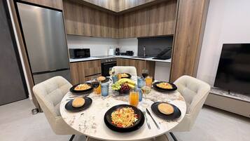A modern kitchen with a dining table set for a meal, including plates of food, glasses, and a fruit bowl.
