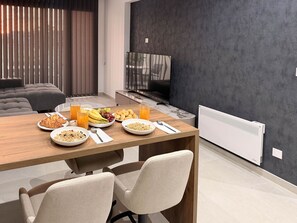 Een moderne eetruimte met een houten tafel gedekt voor het ontbijt, inclusief kommen met ontbijtgranen, fruit en gebak.