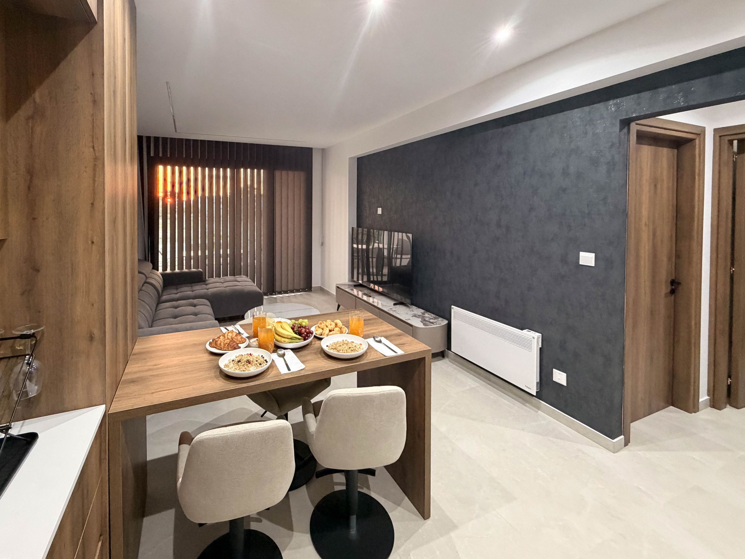 A modern dining area with a wooden table, two chairs, and a sofa in the background.