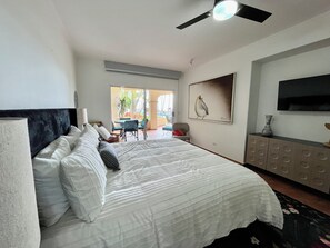 Et soveværelse med seng, ventilator, TV og udsigt til en udendørs patio.