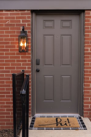 A brown door with a keypad lock, a black mailbox, and a lit lantern on a brick wall. - Stylish Ranch -Wooded Lot in North Indianapolis (Indianapolis)