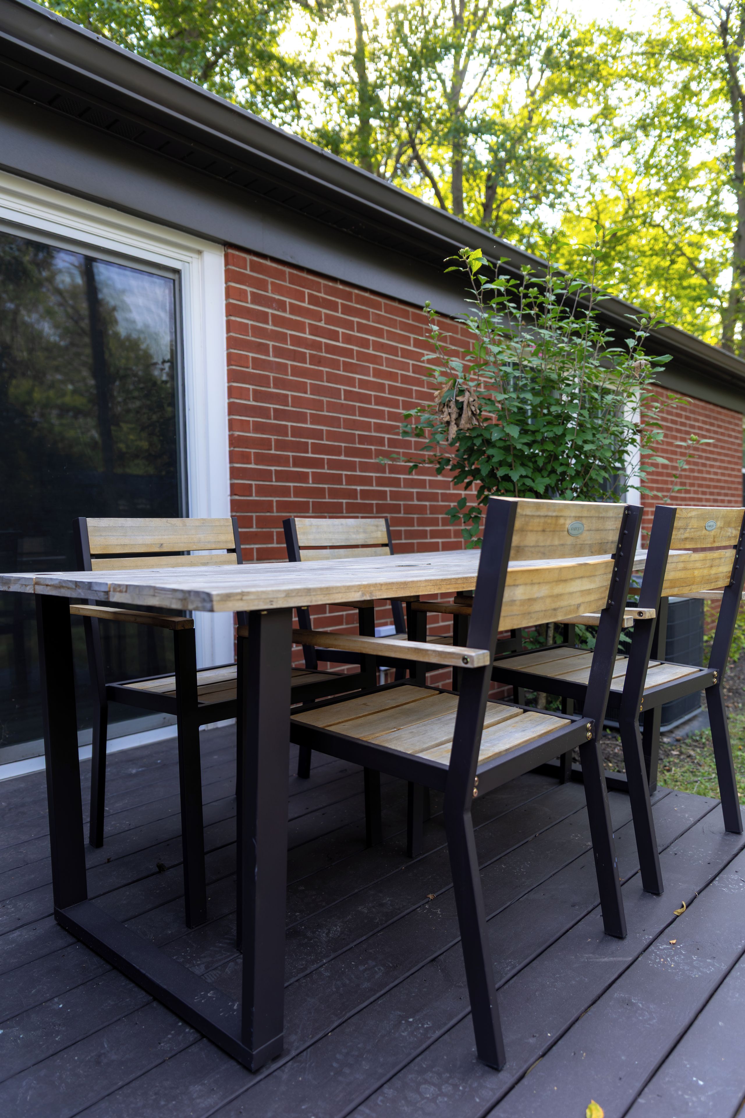 An outdoor seating area with a table and chairs, a brick wall, and a window.