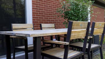 An outdoor seating area with a table and chairs, a brick wall, and a window.