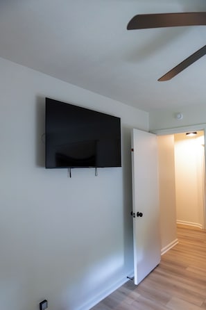 A room with a flat-screen TV mounted on the wall, a door, and a wooden floor. - Stylish Ranch -Wooded Lot in North Indianapolis (Indianapolis)