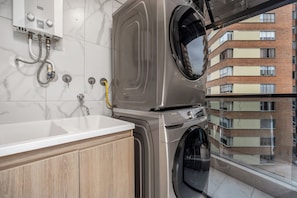 A modern apartment with a built-in washer and dryer, a white marble-tiled wall, and a view of a multi-story building. - Brand New Luxury Apartment with AC (Medellín)