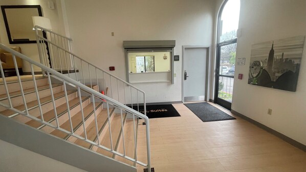 Un hall d’hôtel avec un escalier, une porte, une fenêtre et un paillasson.