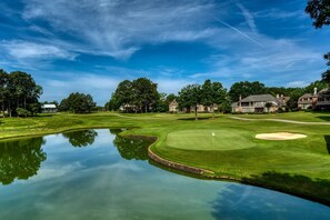 Un parcours de golf avec un étang, des maisons et des arbres.