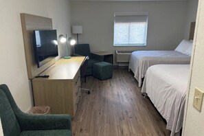 Quarto de hotel com uma cama, uma mesa com computador, uma cadeira, uma televisão e uma janela.