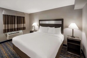 Ein Hotelzimmer mit einem großen Bett, zwei Nachttischen mit Lampen, einem Fenster mit Vorhängen und einer Wand-Klimaanlage.