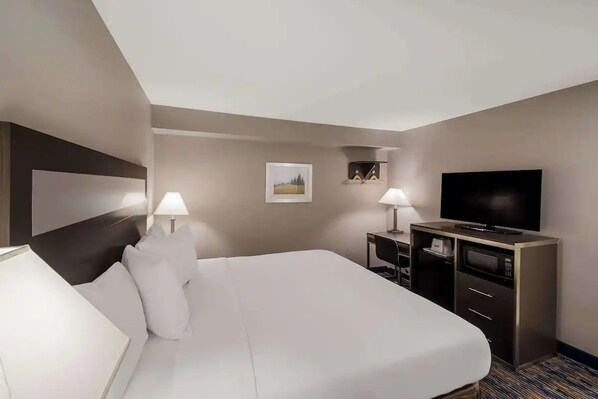 Ein Hotelzimmer mit einem großen Bett, einem Flachbildfernseher, einem Schreibtisch mit Lampe und einer Mikrowelle.