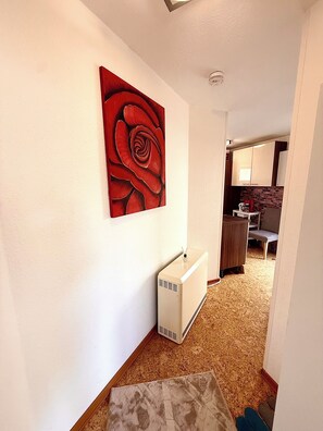 A hallway with a radiator, a red artwork on the wall, and a glimpse of a kitchen area. - Comfortable and worry-free living (Hofheim)