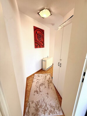 A narrow hallway with a white radiator, a red abstract painting on the wall, and a door with a white frame. - Comfortable and worry-free living (Hofheim)
