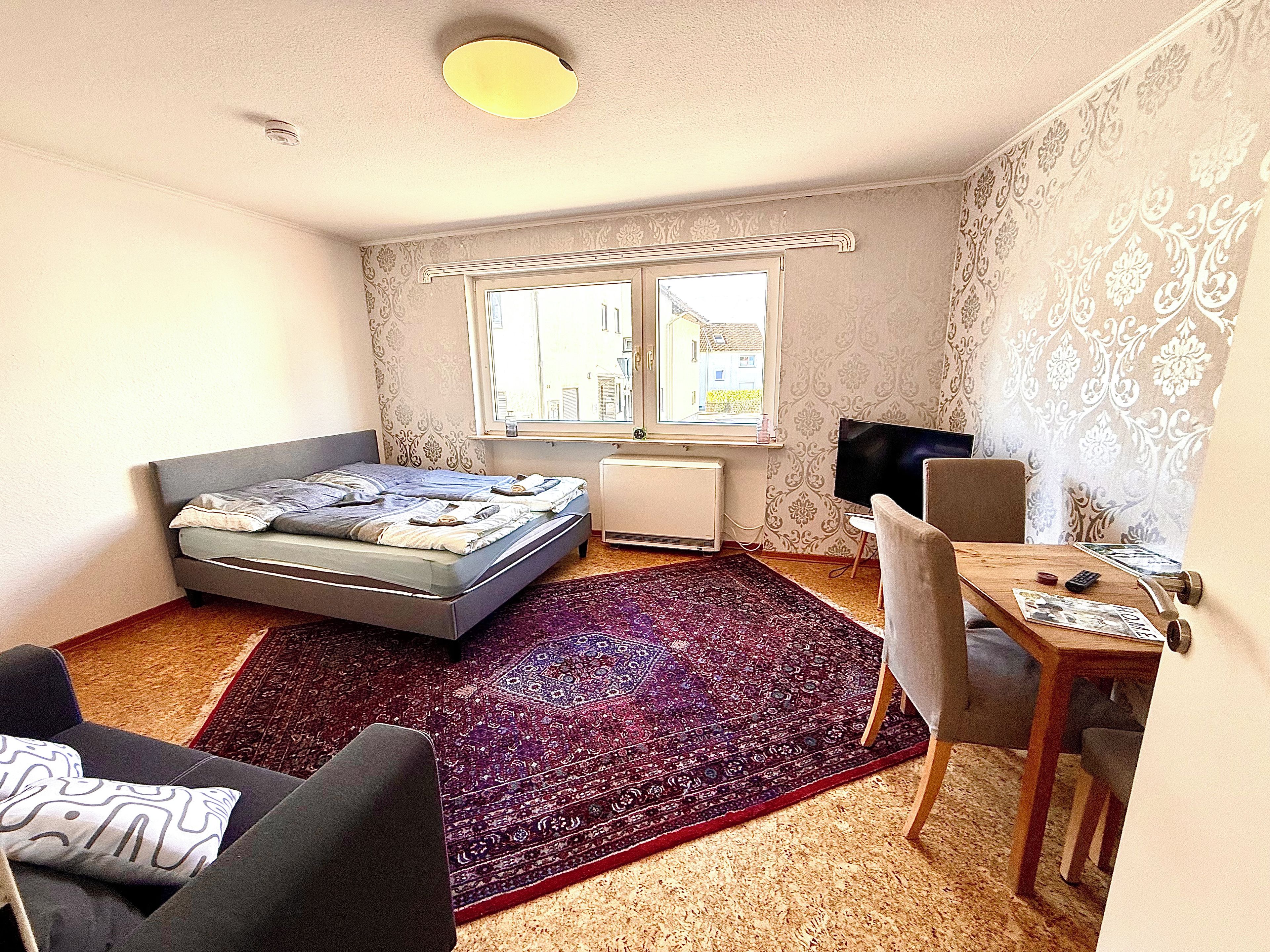 Un dormitorio con cama, escritorio, silla, televisor y ventana.