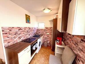 Ett kompakt kök med en väggbeklädnad av tegel, en inbyggd ugn, en tvättmaskin och en kaffemaskin.