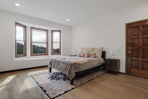 A bedroom with a bed, a nightstand, a wooden door, and a window with a view.
