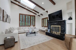 A spacious living room with a fireplace, a large flat-screen TV, and a sofa set.