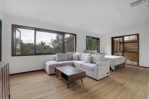 A spacious living area with a sectional sofa, a wooden coffee table, and large windows offering a view of greenery.