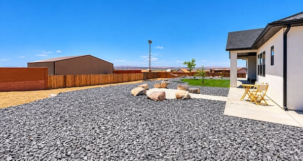 Un jardin avec une zone recouverte de gravier, une clôture en bois et un bâtiment doté d’un toit plat.
