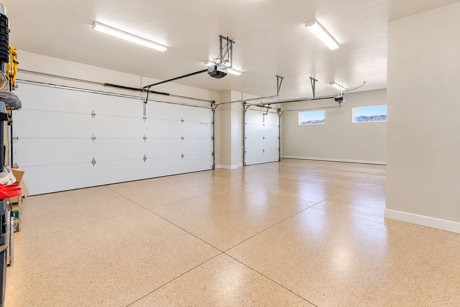 Un garage spacieux avec une grande porte blanche, un éclairage au plafond et une vue dégagée sur l’extérieur grâce à une fenêtre.