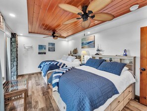 A bedroom with two beds, a ceiling fan, a fireplace, and nautical-themed decor. - Honolii Hale - Oceanfront (Hilo)