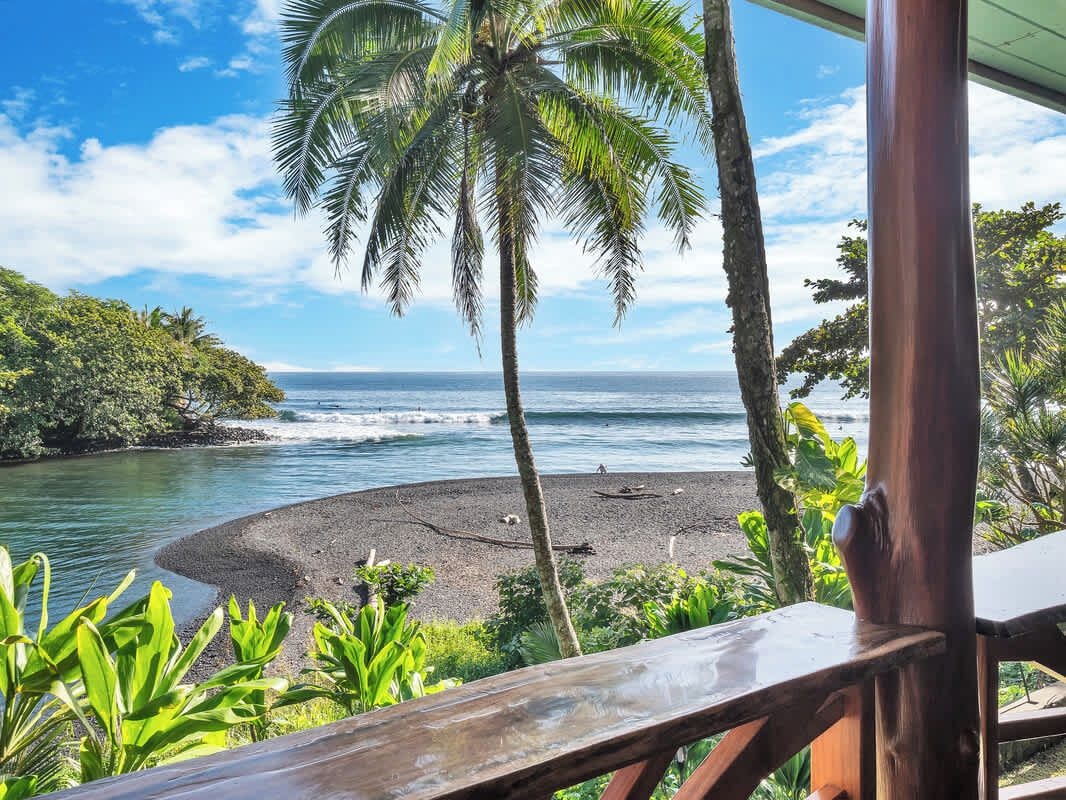 A beach with a wooden deck overlooking the ocean, surrounded by tropical vegetation.