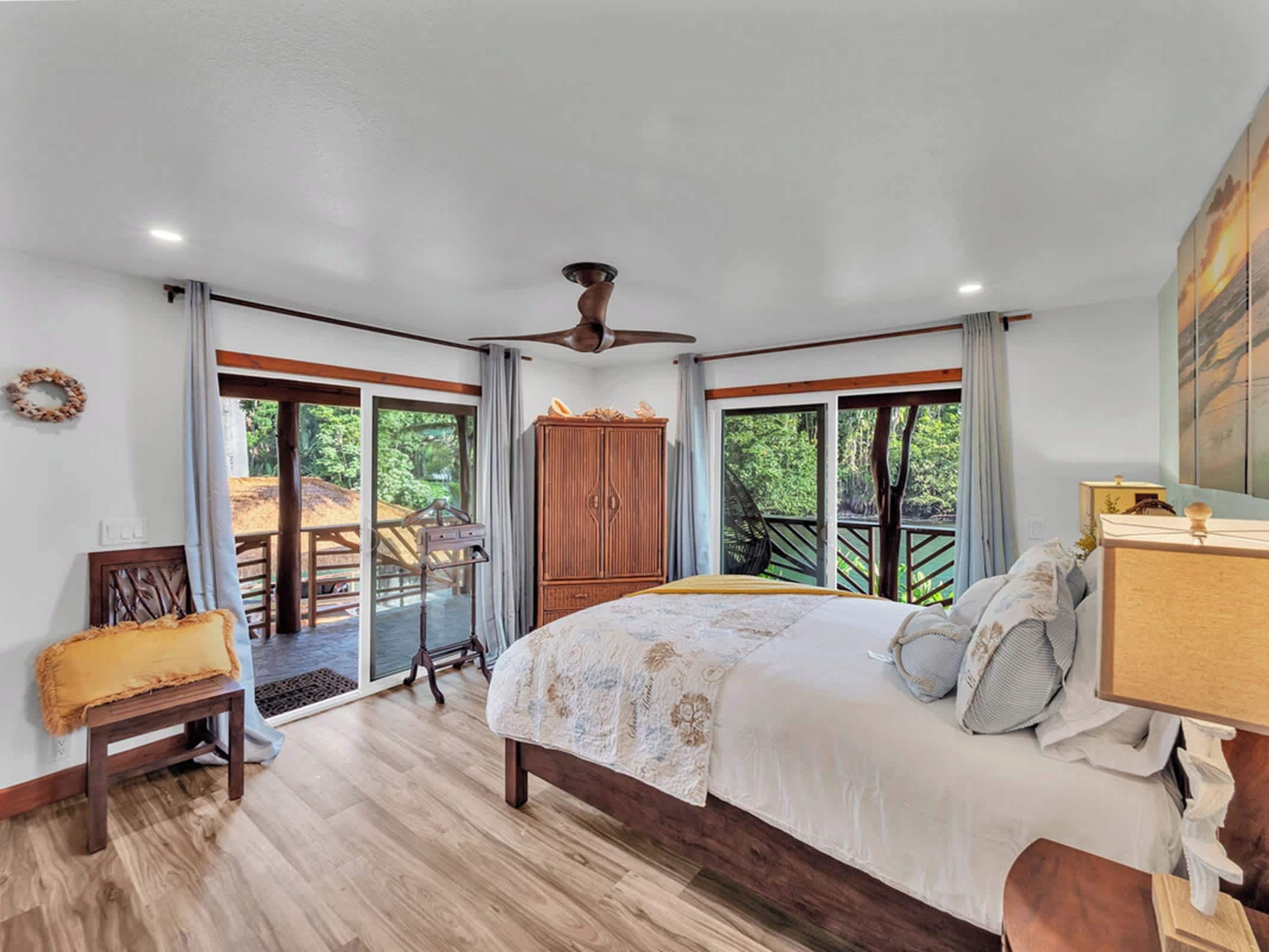 Un dormitorio con una cama grande, ventilador de techo y vista a una terraza de madera.