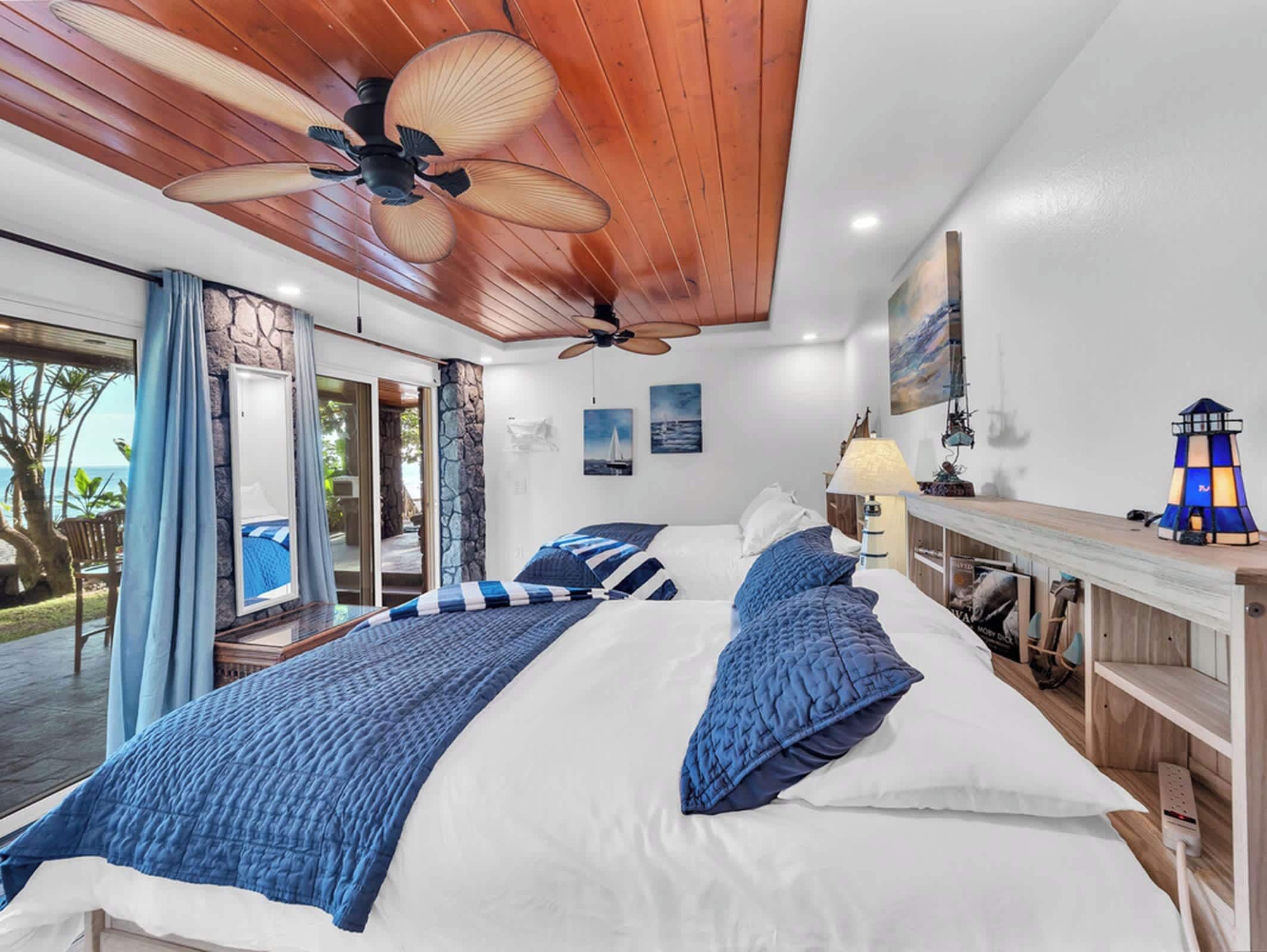 Un dormitorio con una cama grande, un ventilador de techo, un escritorio con lámpara y vistas al exterior.