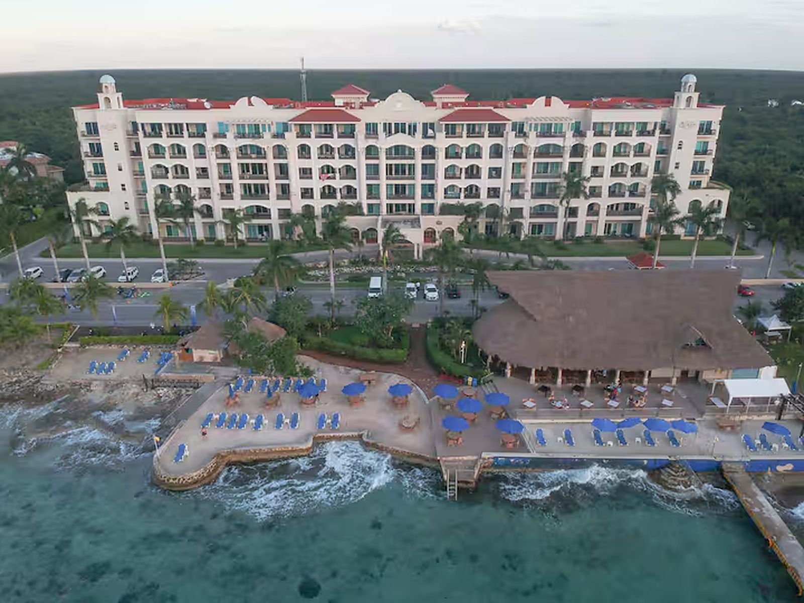 Ein großes Hotel mit mehreren Balkonen, einem Poolbereich mit Sonnenschirmen und Blick auf den Strand.