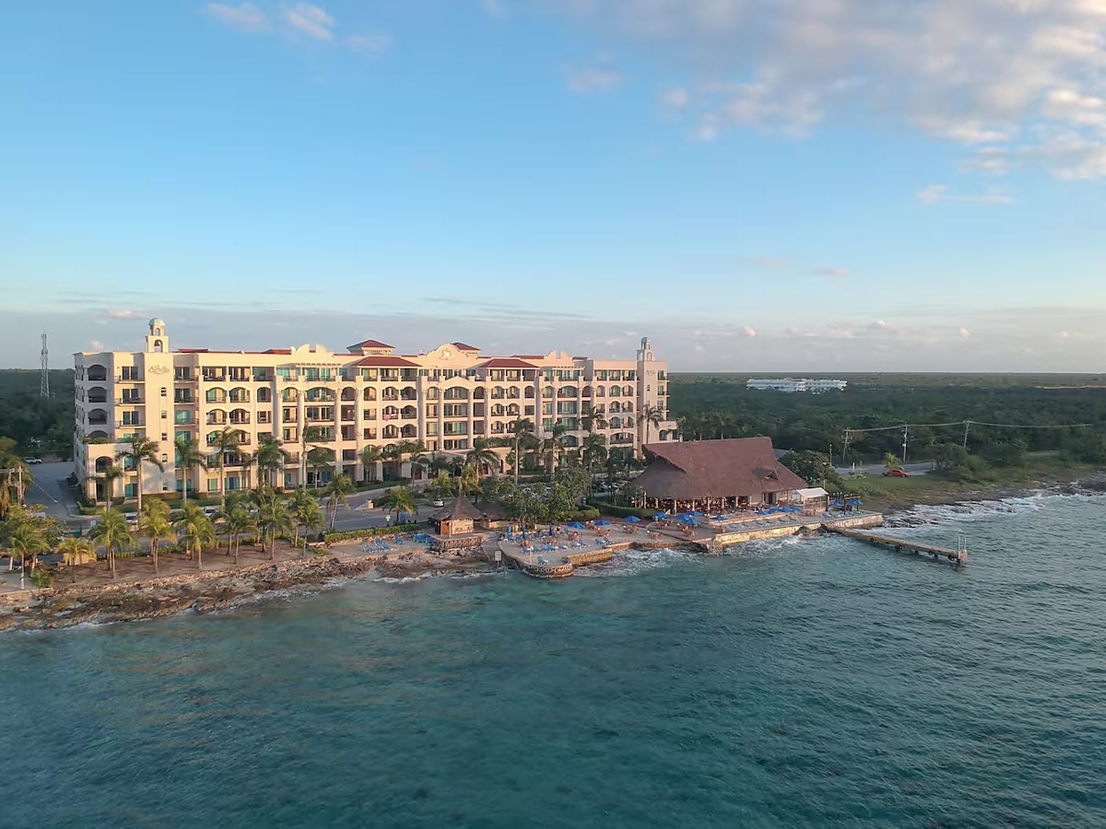 Un grande hotel con numerosi balconi, posizione sul lungomare e un molo che si protende nell'acqua.