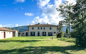 A two-story building with a tiled roof, a red door, and a lawn in front. - Amazing home in Cortona with private swimming pool, can be inside or outside (Cortona)