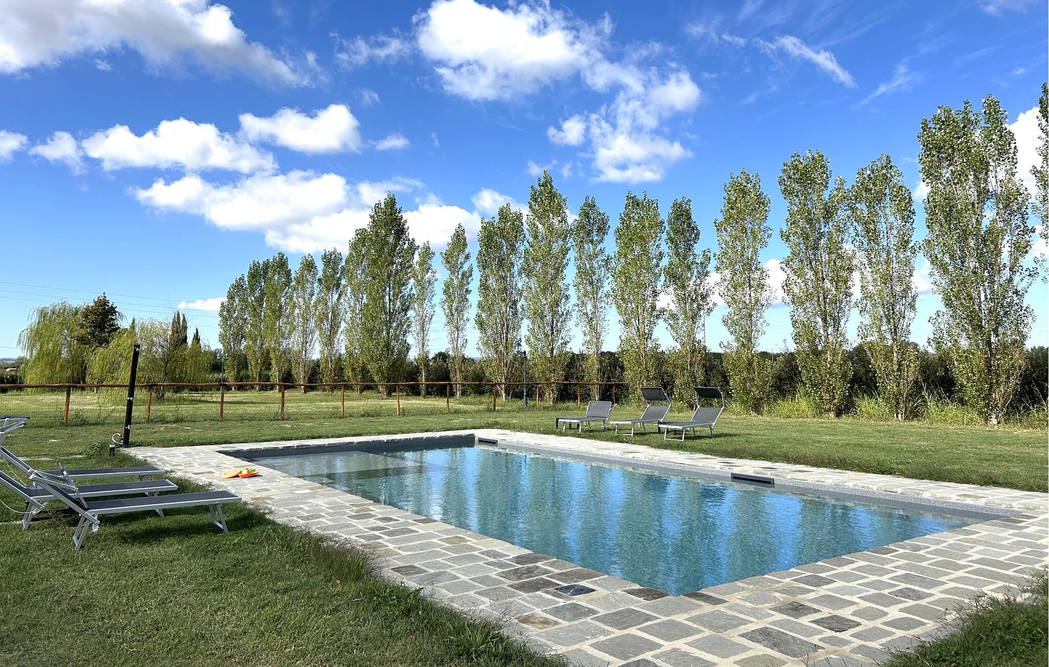 A swimming pool with a stone border, surrounded by grass and trees.