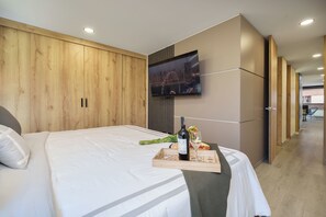 Habitación de hotel con cama, televisor montado en la pared y una bandeja con una botella y vasos.