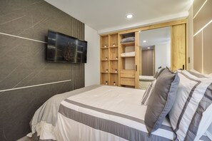 A bedroom with a bed, a television mounted on the wall, and a wooden wardrobe with a mirror. - Brand New Cozy Gem & Luxury Living with AC (Medellín)