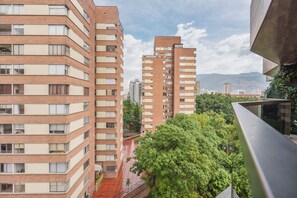 A multi-story residential building with balconies, a red-tiled roof, and a view of a cityscape with mountains in the distance. - Brand New Cozy Gem & Luxury Living with AC (Medellín)