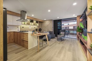 Cocina moderna con isla central, comedor con sofá y sillones, y un amplio ventanal con vistas a la ciudad.