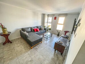 Ein Wohnzimmer mit grauem Ecksofa, einem Glastisch und einem Beistelltisch mit Pflanze.