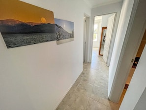 Ein Flur mit einem Landschaftsbild, gefliestem Boden und einer Tür zu einem anderen Raum.