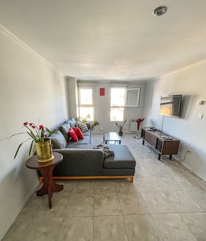 Ein Wohnzimmer mit einer Couch, einem Couchtisch, einem Beistelltisch mit Pflanze und einem an der Wand montierten Fernseher.