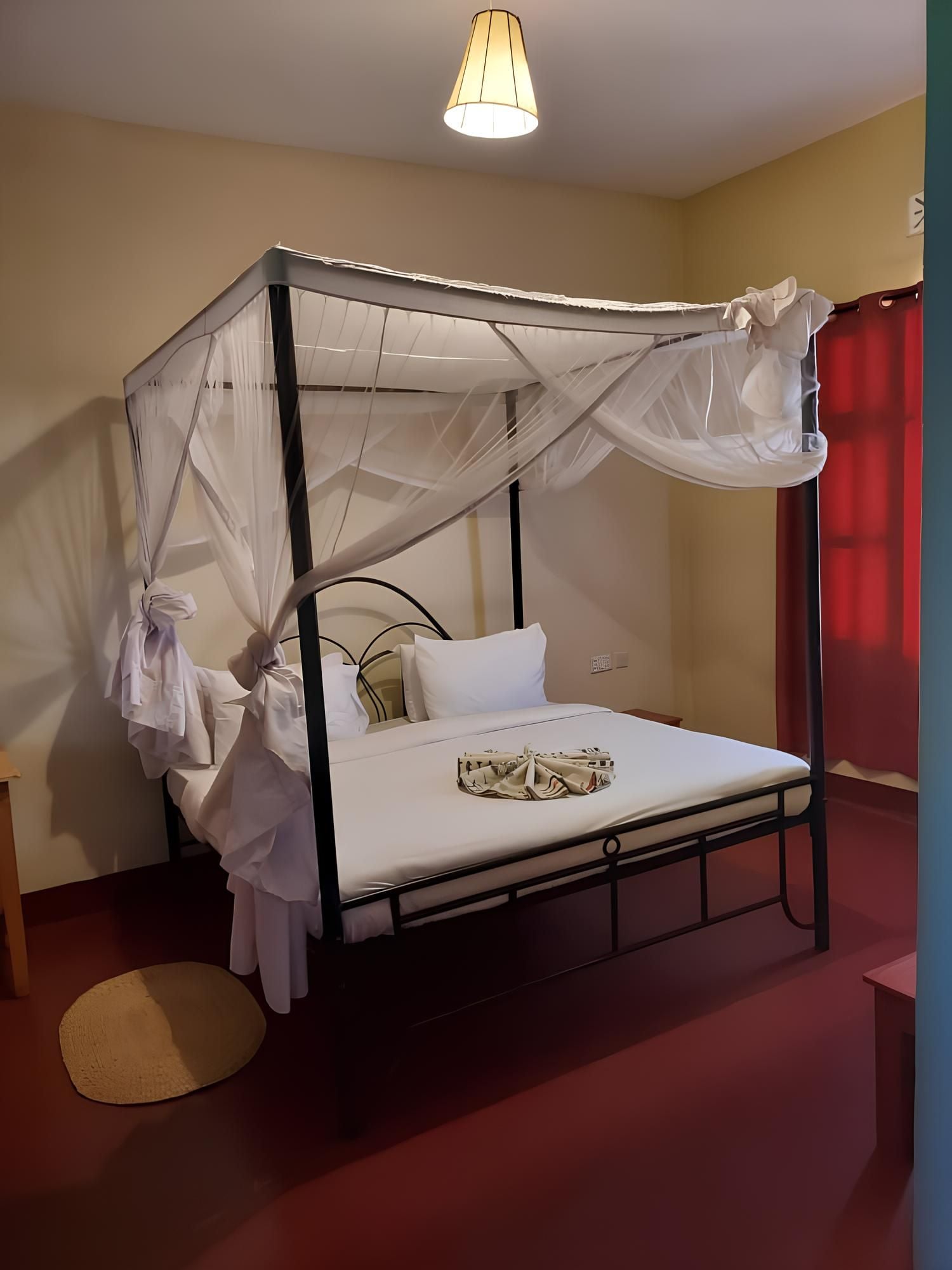 Una cama individual con dosel, una mesita de noche redonda y una cortina roja.