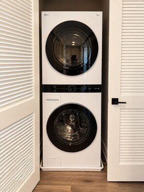A front-loading LG ThinQ washer and dryer unit in a hallway with a wooden floor and white walls. - 2-bedroom furnished luxury apartment Huntley Crossing (Huntley)