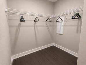 A corner closet with a white wire shelf and multiple black hangers. - 2-bedroom furnished luxury apartment Huntley Crossing (Huntley)