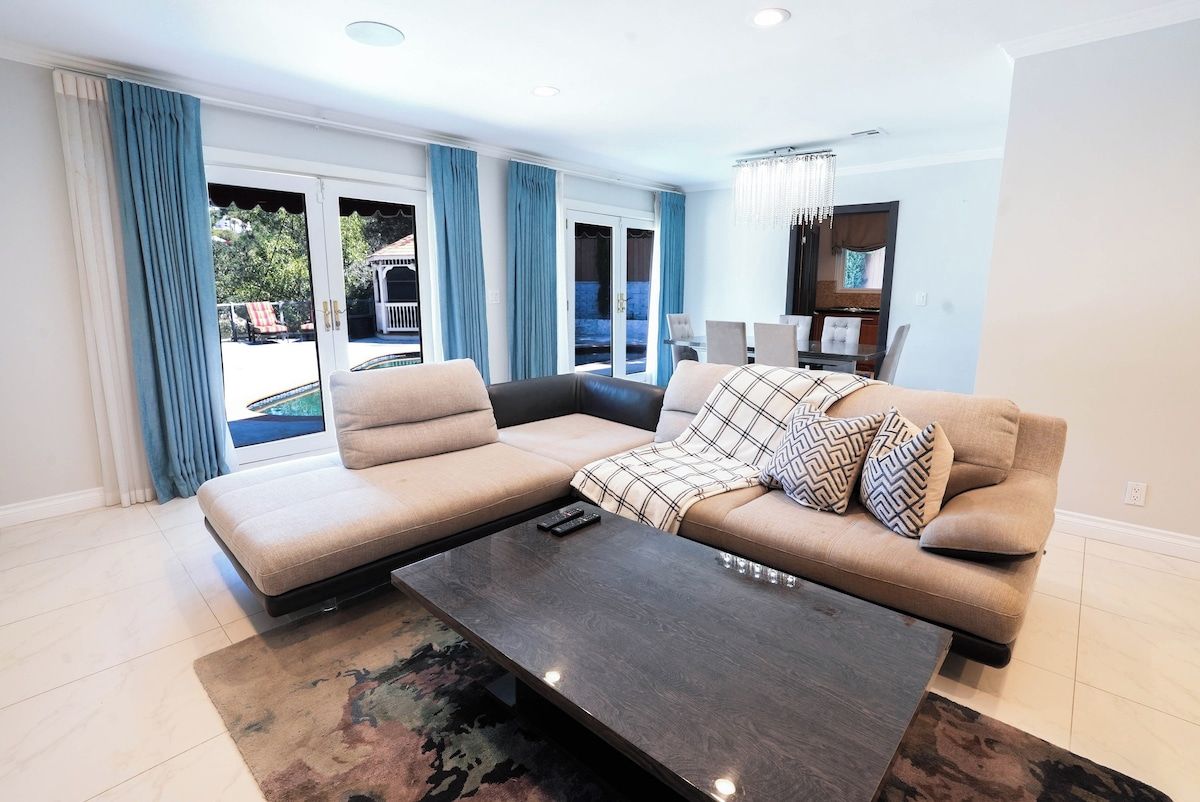 A modern living room with a sectional sofa, a coffee table, and a view of a pool through glass doors.