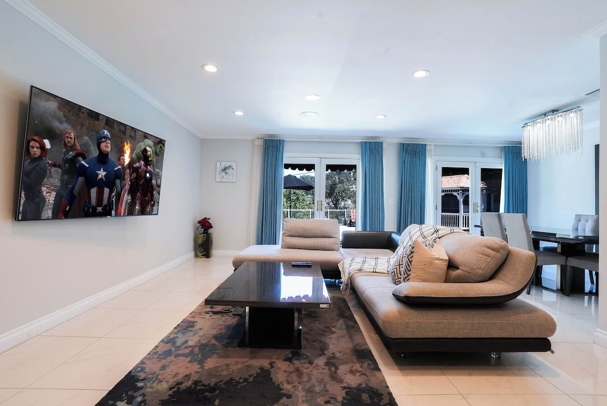 A modern living room with a sofa, armchairs, a coffee table, and a large flat-screen TV mounted on the wall.