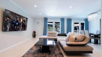 A modern living room with a sofa, armchairs, a coffee table, and a large flat-screen TV mounted on the wall.