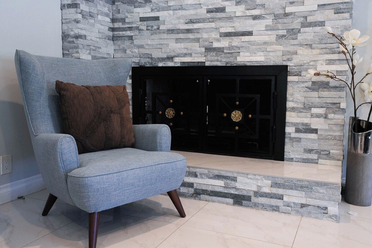 Una sala de estar moderna con chimenea de piedra, un sillón azul y un jarrón con flores blancas.