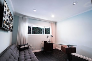 Una sala de estar moderna con un escritorio de vidrio, un sofá acolchado y un amplio ventanal con cortinas.