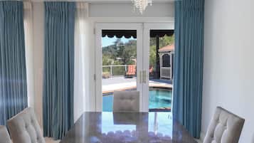 A dining area with a glass table, chairs, and a view of a swimming pool and outdoor seating.