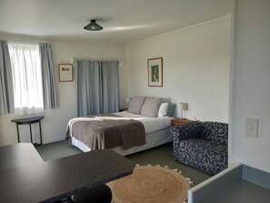 A bedroom with a bed, bedside table, lamp, chair, and a small table.