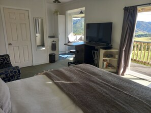A hotel room with a bed, a desk, a TV, and a balcony with a view of the mountains.